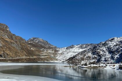 Tsomgo Lake with clear water surrounded by sandy, snowy shorelines and partial greenery