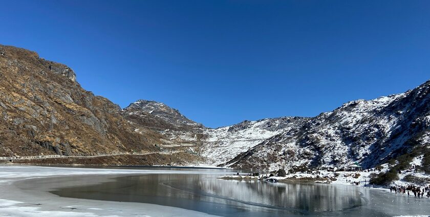 Tsomgo Lake with clear water surrounded by sandy, snowy shorelines and partial greenery