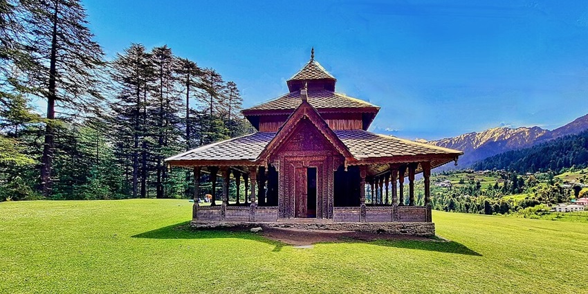 A temple with old architecture in a valley full of greenery surrounded by mountains.