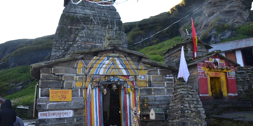 View of the temple building with rugged mountains in the back and lush greenery