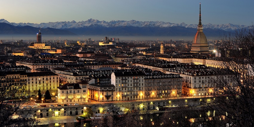 Turin skyline at dusk, featuring the Mole Antonelliana and the Alps in the background.