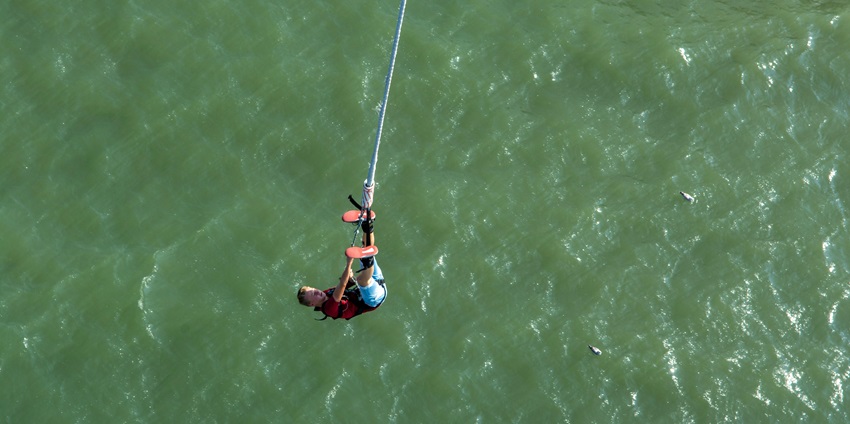 A person hanging upside down from a rope over waters, resembling Udaipur bungee jumping