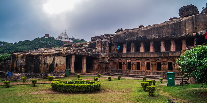 An image of Udayagiri and Khandagiri caves with a manicured garden in the foreground and a temple in the background