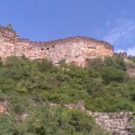 Ancient stone walls of Udayagiri Fort rising atop a lush green hill under a clear sky