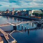 An Image of Dublin city featuring modern buildings, a river, and a bridge under a blue sky.