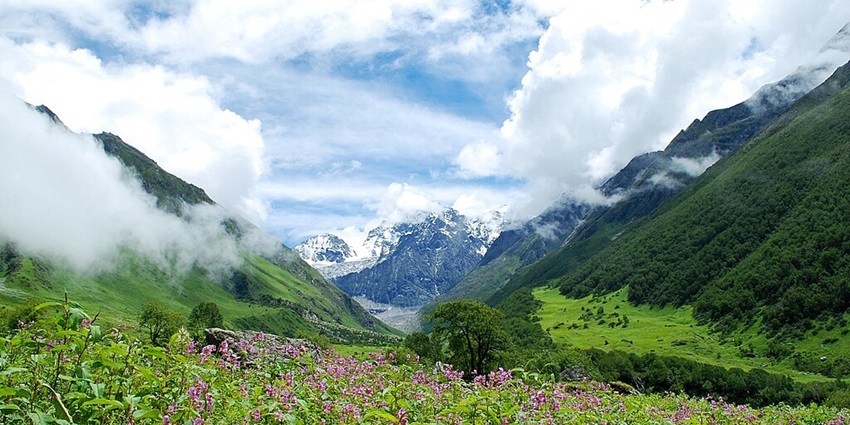 An image of a vast snow-capped mountain range under a clear sky with scattered clouds