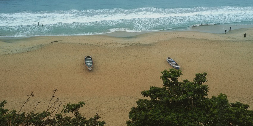 An image of boats and waves crashing on Varkala beach, with people swimming and relaxing