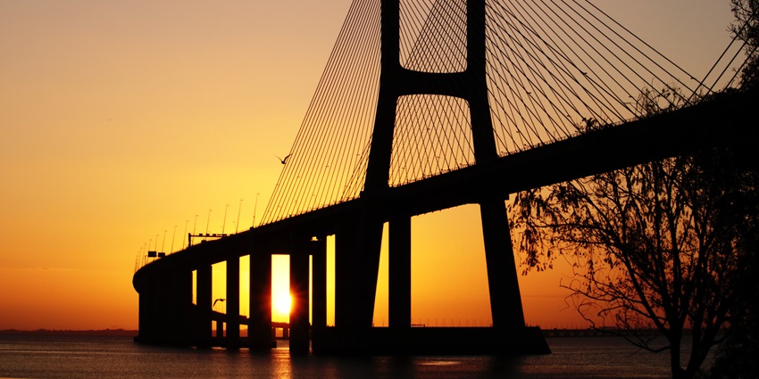 A setting Sun peeks through the pillars of the Vasco da Gama Bridge in Lisbon, Portugal.