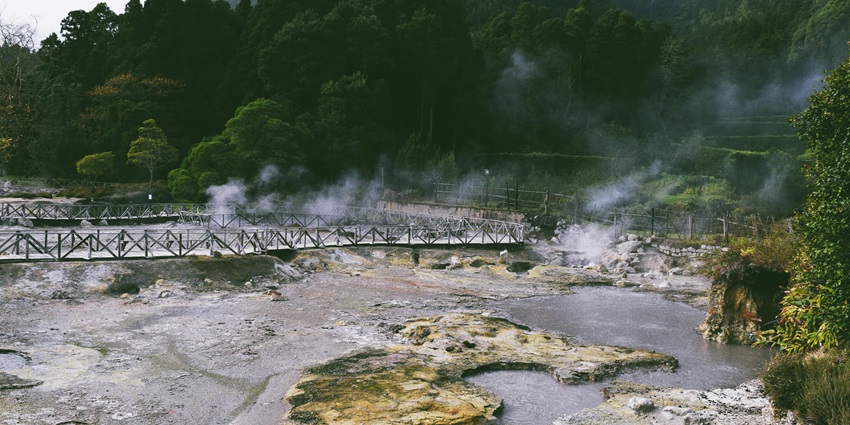 A hot spring surrounded by lush green mountains, with steam rising from the rocky terrain