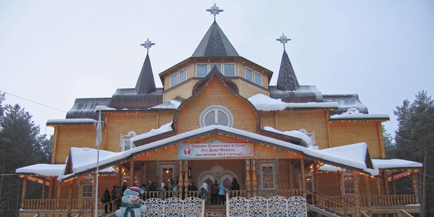 A large wooden house with pointed towers, decorated for winter with snow and a snowman