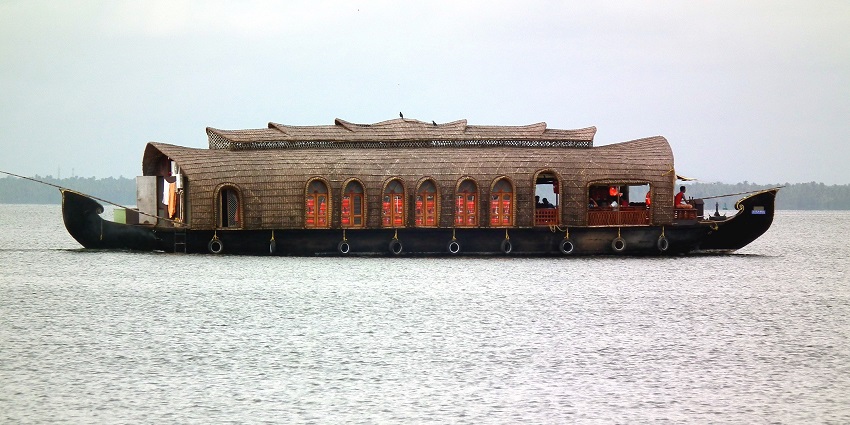 One houseboat with multiple windows and people inside the boat on the Vembanad Lake.
