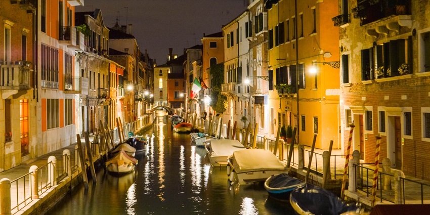 Venice canal at night, with illuminated buildings, boats, and reflections on the water