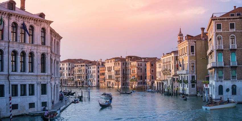 Image of a man sitting on a chair on a small overbridge above a canal in Italy’s Venice.