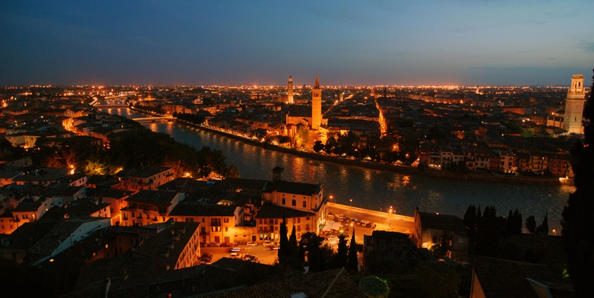 An image of Verona at night, with the Adige River winding through the illuminated city.