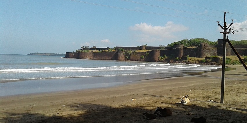 An image of the Vijaydurg fort with a view of waves hitting the shore, a sandy beach