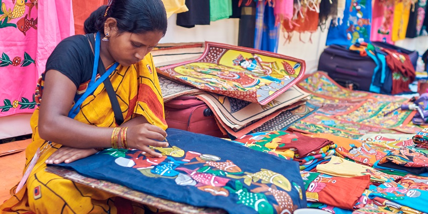 Alt Text: A rural craft-woman belonging to development communities, painting tribal fish motifs.