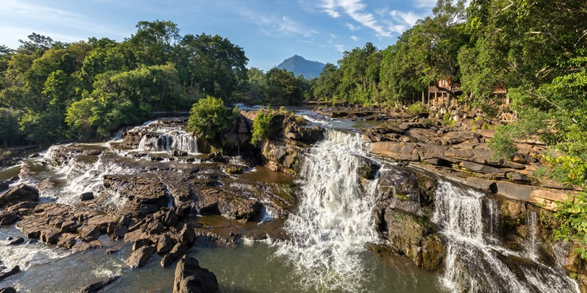 A picture of a quaint waterfall with water cascading down the rocks into a pond of water
