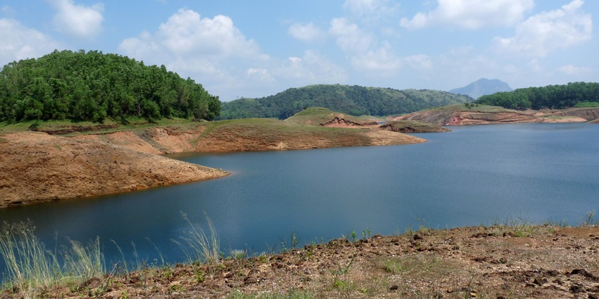 Dam reservoir lake with sandy shorelines and small hills covered with green trees.