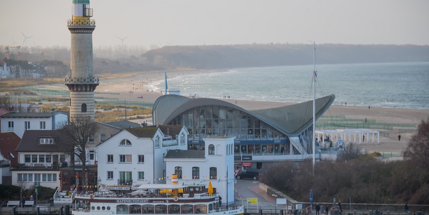 An image showing the Warnemünde Lighthouse overlooking the sandy beach under a clear sky.