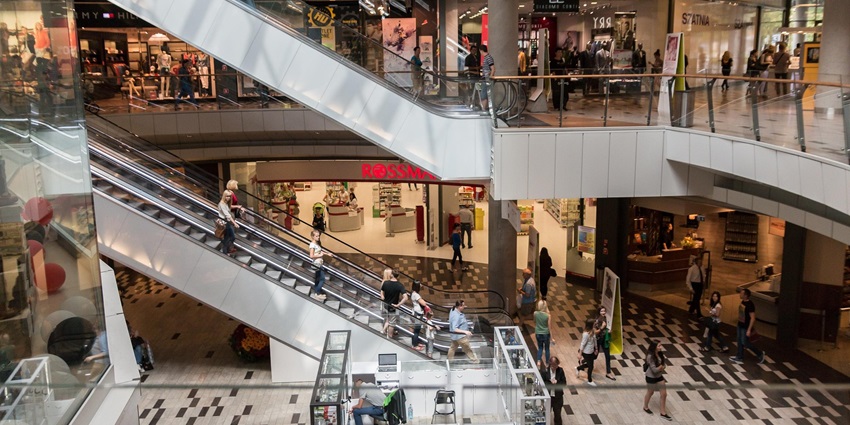 An image of a bustling shopping mall with escalators and stores on multiple levels.