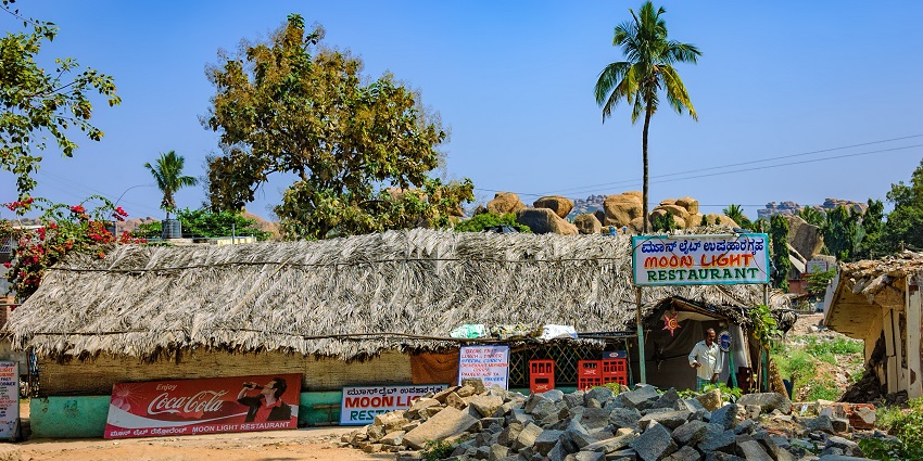 Restaurant made of mud houses with a thatched roof, palm trees and piles in Hampi, India