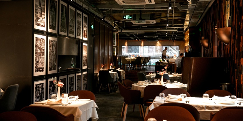 Image of a restaurant interior with set tables, artwork on the walls, and a waiter.