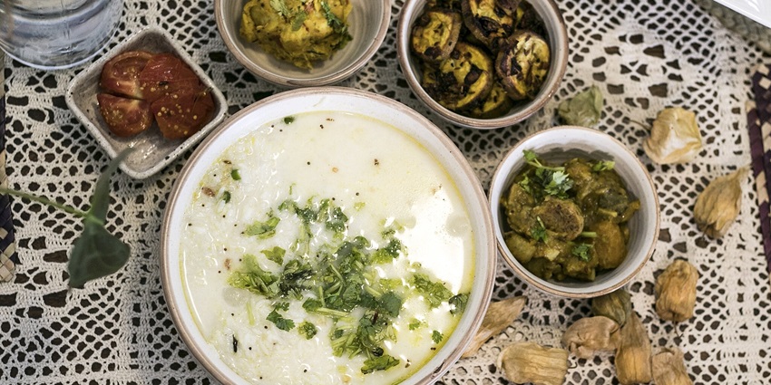 Pakhala served in a bowl with barbecued tomatoes, cooked vegetables and other side dishes