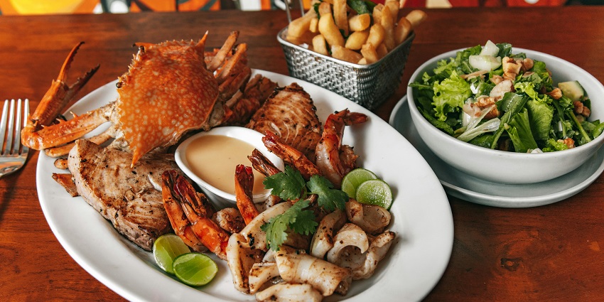 A plate of seafood and other dishes, including crab, and a salad, on a wooden table
