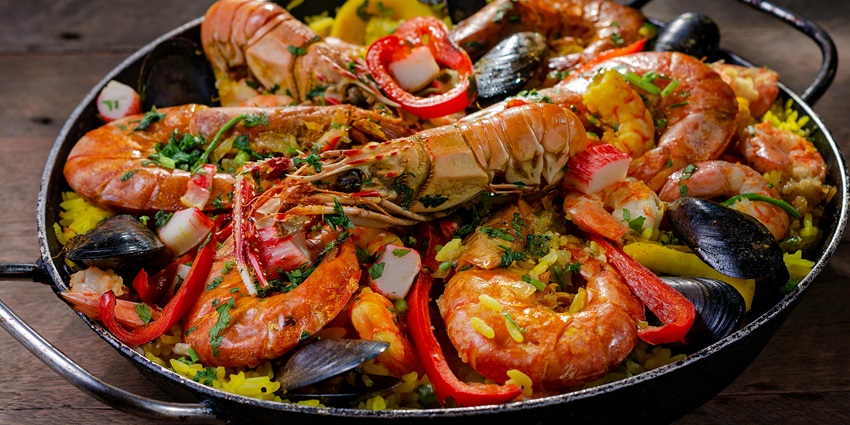 A pan of seafood paella with shrimp, and other shellfish, garnished with red peppers