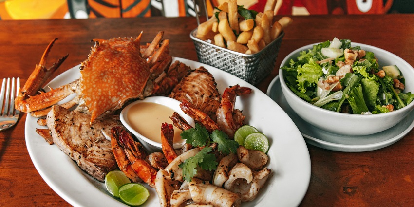 A seafood platter with grilled shrimp, fish, crab, and squid, served with salad, fries