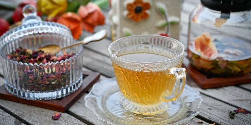 Kashmir style kahwa served in a cup next to a pot with flowers and a bowl with spices