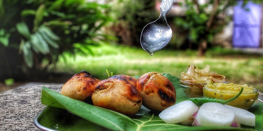 Litti chokha served on a leaf with salad on the side and ghee dripping from the spoon