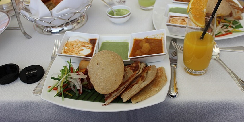North Indian food thali with puri, multiple chutneys and salad served on a white plate