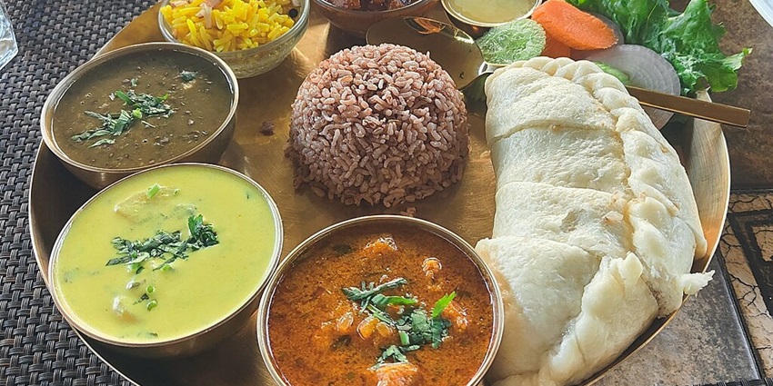 Traditional Himachali thali with brown rice, multiple curries and salad served on a plate.