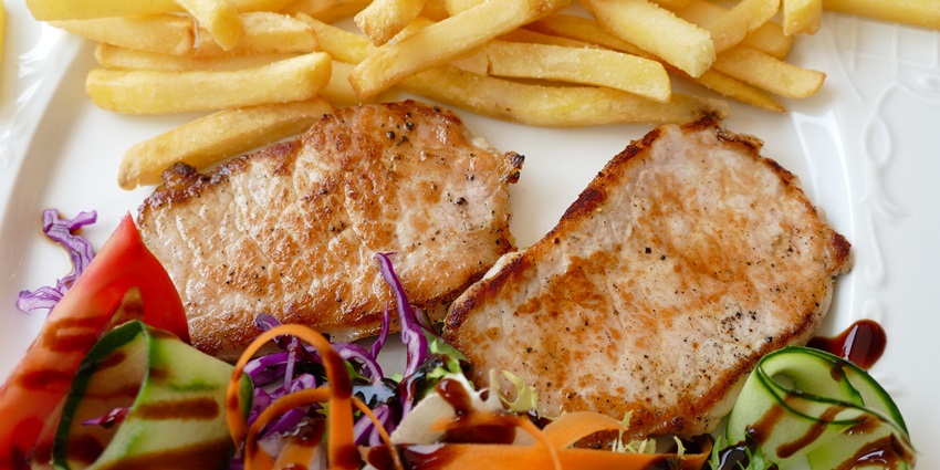 Two pork chops and french fries on a white plate, garnished with a salad of tomato