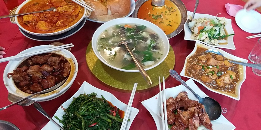 A table laden with dishes, including curries, vegetables, and meat, with people eating.
