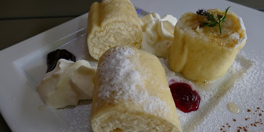Sliced štruklji pastries dusted with powdered sugar, served with whipped cream and fruit