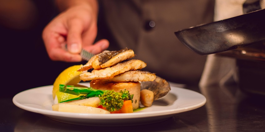 A dish of pan-seared fish fillets with vegetables and a lemon wedge on a white plate.