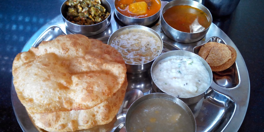 A plate containing puri, curries in bowls, and sweets, arranged for a traditional meal