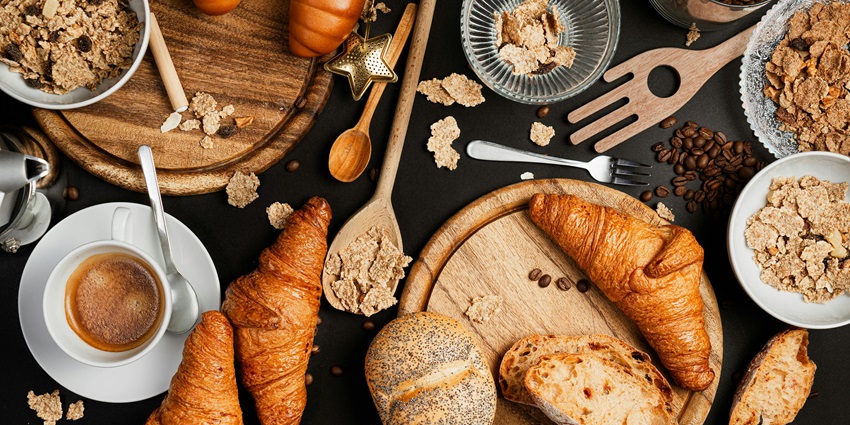A flat lay of breakfast items including croissants, cereal, coffee bread, and coffee