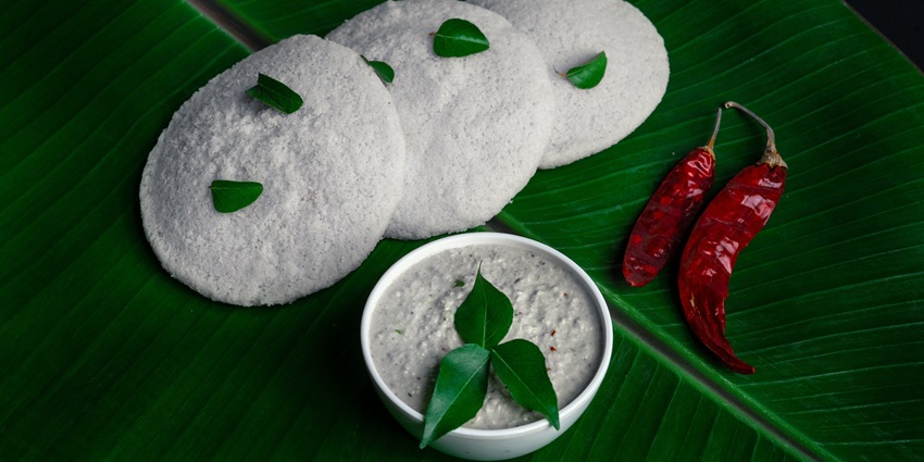 Three idlis garnished with curry leaves, served on a banana leaf with coconut chutney
