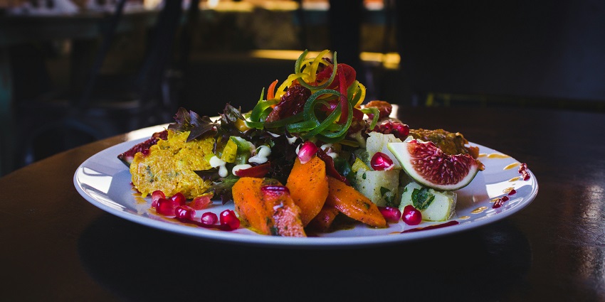 Vegetable salad garnished with pomegranate has been placed on a restaurant table.