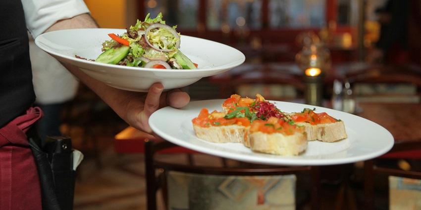 Image of a person holding pastry and dishes on a ceramic plate in the restaurant