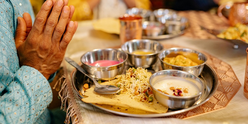 A person praying before a table filled with various dishes, hands clasped in gratitude