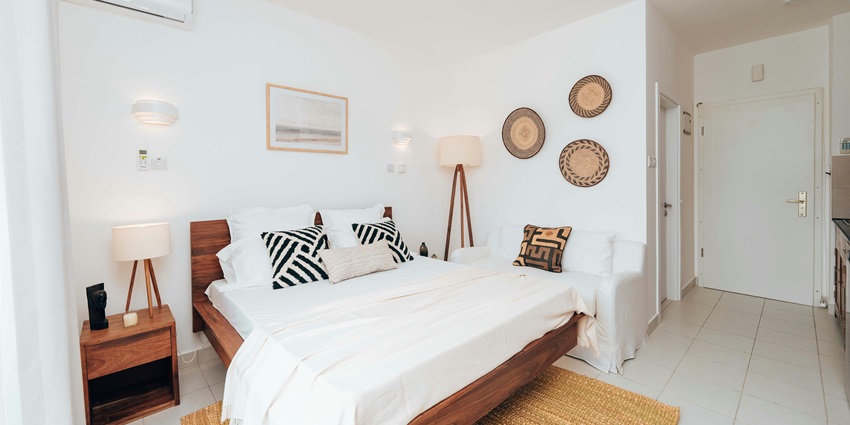 Luxury white-themed studio apartment with a neatly made bed and wooden furniture