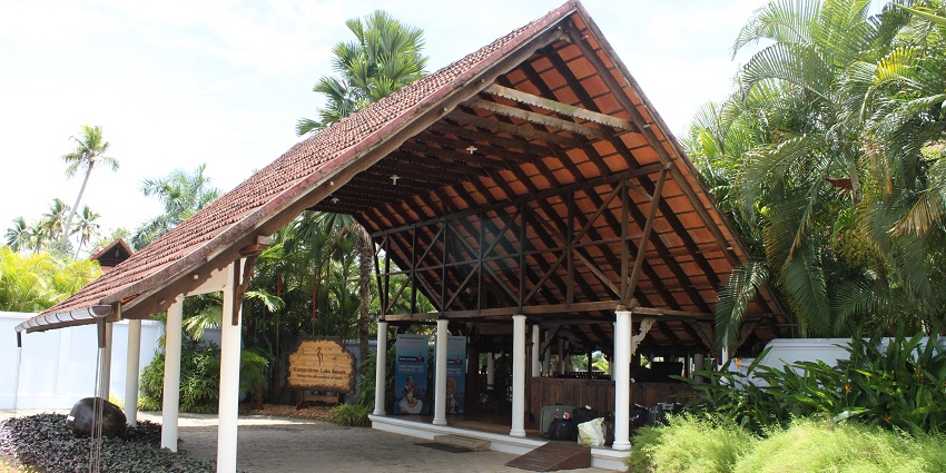 Shed of the Kumarakom Lake resort entrance gate surrounded by palm trees and greenery.