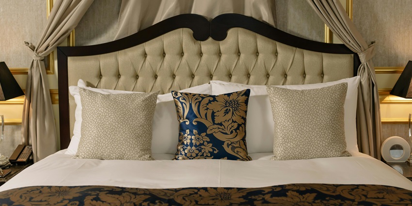 Neatly made bed in a hotel room with white sheets, multiple pillows near Manasbal Lake in Kashmir.