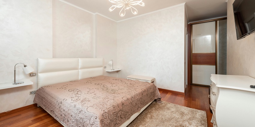 A contemporary bedroom featuring a large bed, hardwood floors, and sliding closet doors.