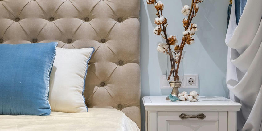 A light beige headboard with two pillows resting against it, beside a white nightstand