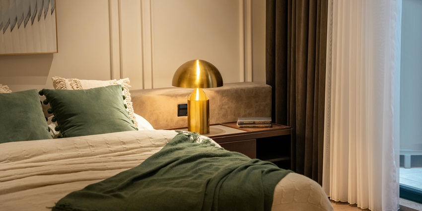 A neatly made bed with a beige comforter, green throw blanket, and decorative pillows